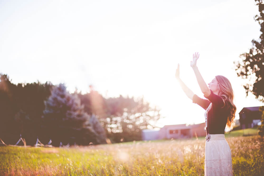 woman with raised arms standing in field looking towards sky